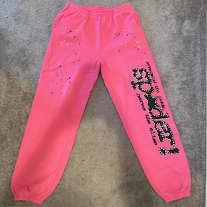Puede incluir: Pantalones deportivos de color rosa brillante con un diseño de constelación y el texto "Spider!" en la pierna izquierda. El texto "nevermind the punk, bores the bliss" está impreso verticalmente en la pierna izquierda. Los pantalones tienen cintura y puños elásticos.