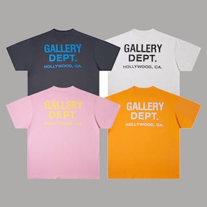 Könnte beinhalten: Vier kurzärmelige T-Shirts in verschiedenen Farben: Marineblau, Hellgrau, Rosa und Orange. Jedes Shirt zeigt den Text "GALLERY DEPT. HOLLYWOOD, CA." in einer Kontrastfarbe auf der Rückseite.