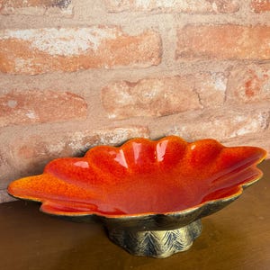 May include: A scalloped bowl with a vibrant orange and red gradient interior finish. The exterior of the bowl and its pedestal base feature a dark, textured metallic finish with visible brush strokes, creating a contrast with the smooth, glossy interior.