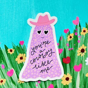Puede incluir: Una pegatina caprichosa que presenta un fantasma con un sombrero de vaquero rosa. El fantasma est&aacute; cubierto de peque&ntilde;os estampados florales y tiene ojos en forma de coraz&oacute;n. El texto "you're a cowboy like me" est&aacute; escrito en el fantasma. El fondo incluye flores y hierba verde.