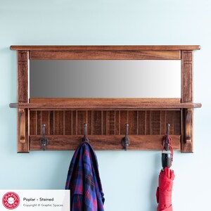 May include: A stained wood wall mounted coat rack with a mirror above it. The rack has four hooks and a shelf. The mirror is rectangular and has a wooden frame. The text "Poplar - Stained" and "Copyright &copy; Graphic Spaces" is visible below the rack.