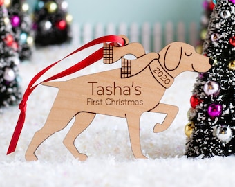 Könnte beinhalten: Ein hölzerner Weihnachtsbaumschmuck in Form eines Hundes, der einen Schal trägt. Der Anhänger ist mit dem Namen "Tasha's" und dem Text "First Christmas" sowie dem Jahr "2020" personalisiert.