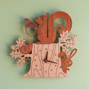 May include: A wooden wall clock shaped like a tree with a squirrel, snail, rabbit, and birds. The clock face has Roman numerals and a brown hand.