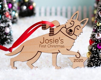 Könnte beinhalten: Ein hölzerner Weihnachtsbaumschmuck in Form eines Hundes, der einen Stern hält. Der Hund trägt einen Schal und der Stern trägt das Jahr 2020. Der Schmuck ist mit dem Text "Josie's First Christmas" personalisiert.