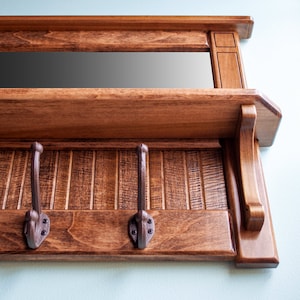 May include: A wooden coat rack with a mirror and three hooks. The rack is stained a dark brown color and has a shelf above the hooks.