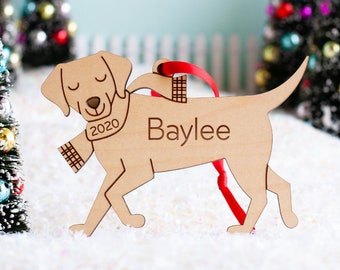 May include: Wooden Christmas ornament shaped like a dog wearing a scarf. The ornament is light brown and has the name "Baylee" and the year "2020" engraved on it.