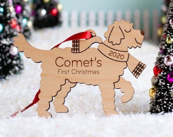 Könnte beinhalten: Ein hölzerner Anhänger in Form eines Hundes, der einen Schal trägt. Der Anhänger ist hellbraun und trägt den Text "Comet's First Christmas" und "2020".