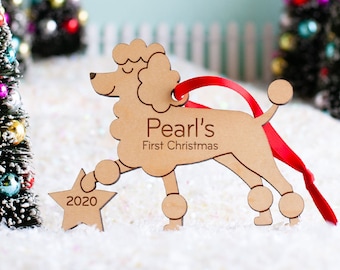 May include: A wooden Christmas ornament shaped like a poodle dog with the text "Pearl's First Christmas" and the year "2020" on a star.