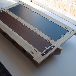 May include: The back of a wooden picture frame with a mirror and a brown backing. The frame is held together with screws and has a few small holes drilled into it.