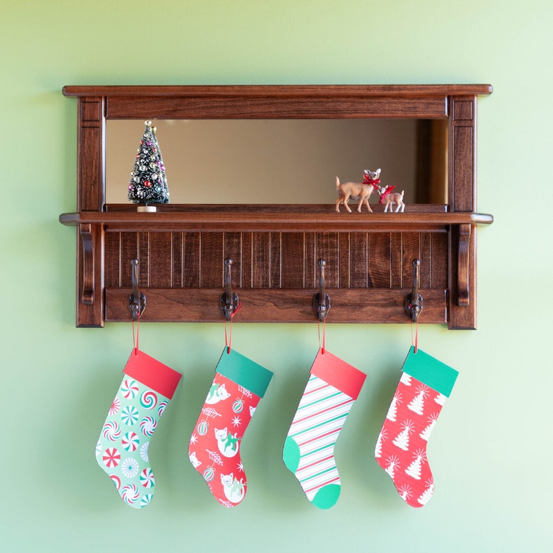 May include: A wooden shelf with a mirror and four hooks. There are four Christmas stockings hanging from the hooks. The stockings are red and green with different patterns. There is a small Christmas tree on the shelf.