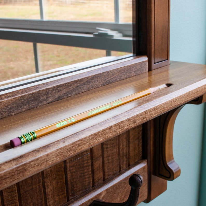 May include: A wooden shelf with a pencil resting in a slot. The shelf is attached to a mirror with a decorative hook.