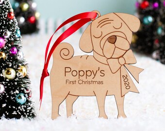 May include: A wooden Christmas ornament shaped like a pug dog with a red ribbon. The ornament is personalized with the text "Poppy's First Christmas 2020".