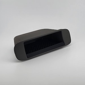 May include: A matte black automotive interior storage tray featuring a rectangular recessed compartment with a textured, non-slip base. The component has rounded edges and a smooth, contoured frame designed for integration into a vehicle dashboard.