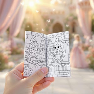 以下が含まれることがあります： プリンセスのイラストが描かれた、小さな開いた塗り絵。一人のプリンセスは本を読んでおり、もう一人はバルコニーから手を振っています。絵は白黒で、背景にはお城があります。本は手で持たれており、背景はぼやけています。