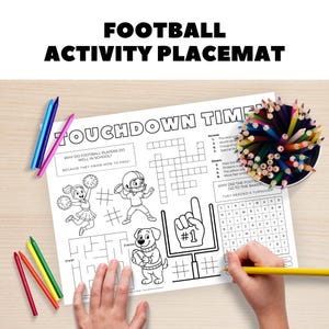 May include: A white football activity placemat with the text "FOOTBALL ACTIVITY PLACEMAT" and "TOUCHDOWN TIME". The placemat features a crossword puzzle, a maze, and illustrations of football players, a cheerleader, and a dog. Colored pencils and crayons are also visible.