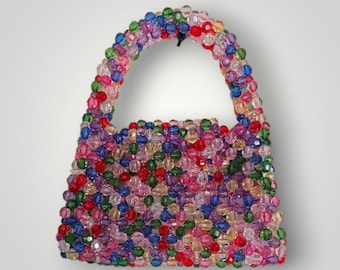 May include: A colorful beaded handbag with a rounded handle. The bag is covered in a variety of small, round beads in shades of red, pink, blue, green, and yellow. The bag is a small, stylish accessory.