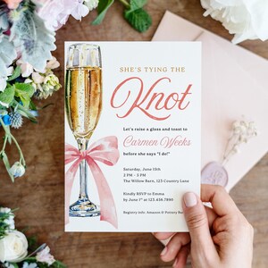Pode incluir: Um convite de casamento com uma ilustração de taça de champanhe e um laço rosa. O texto diz "She's Tying the Knot" e convida os convidados a celebrar Carmen Weeks. Detalhes incluem data, hora e local.