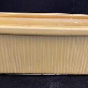 May include: A pale yellow ceramic planter with a rectangular shape and vertical ribbed texture.