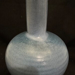 May include: A blue ceramic vase with a rounded body and a tall, narrow neck. The vase has a light blue glaze with a subtle swirl pattern.