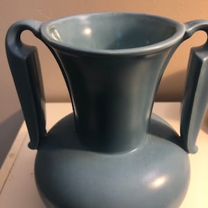 May include: A light blue ceramic vase with two handles. The vase has a rounded body and a flared top.