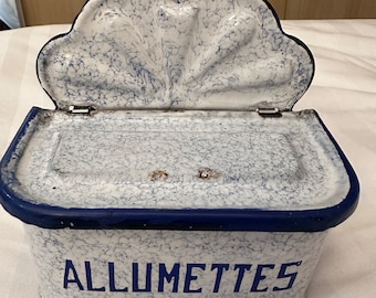 May include: White enamel matchbox with a blue rim and a blue and white marbled pattern. The lid has a decorative scalloped edge and a hole in the center. The box is labeled "ALLUMETTES".
