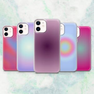 Puede incluir: Cinco fundas transparentes para teléfono con diseños de gradiente coloridos. Las fundas muestran tonos de rosa, morado y azul, con un efecto suave y borroso. Las fundas están dispuestas en fila, mostrando la cámara y los botones del teléfono.