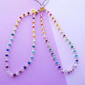 May include: Two necklaces with clear beads and rainbow colored accents. The necklaces are on a purple background.