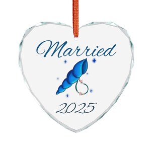 Peut inclure: Ornement en forme de cœur transparent avec le mot « Married » en bleu. Il présente un motif de coquillage bleu avec une bague et l'année « 2025 ». L'ornement a un aspect facetté et un ruban orange pour l'accrocher.