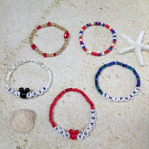 May include: Five beaded bracelets in various colors and designs. One bracelet has the text "DCL 202X" with a Mickey Mouse head. Another says "BON VOYAGE" with a Mickey head. Other bracelets have red, gold, blue, and white beads.