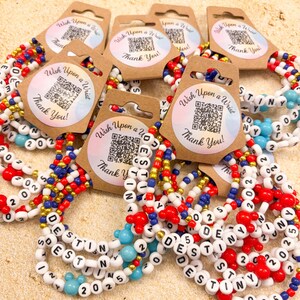 Pu&ograve; includere: Una collezione di braccialetti di perline con il nome "DESTINY" scritto con perline di lettere bianche. I braccialetti presentano perline rosse, bianche, blu e oro, alcune con perline a forma di Mickey Mouse. Ogni braccialetto &egrave; attaccato a un'etichetta con "Wish Upon a Wrist" e "Thank You!"