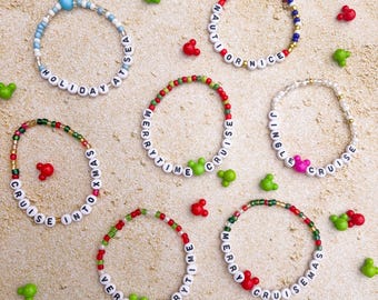May include: A collection of beaded bracelets with white letter beads spelling out phrases like "Holiday at Sea" and "Merrytime Cruise." The bracelets feature colorful beads and Mickey Mouse-shaped accents in red, green, and blue.
