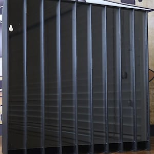 Puede incluir: Un expositor vertical negro con múltiples compartimentos. La caja tiene forma rectangular y está hecha de un material oscuro y translúcido. Los compartimentos están separados por divisores verticales, creando ranuras individuales.