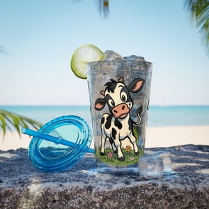 May include: A clear plastic tumbler with a blue lid and straw, featuring a cartoon cow design. The tumbler is filled with ice and a lime wedge. The background shows a beach scene with palm trees and the ocean.