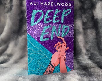 May include: A book cover with the title "DEEP END" in turquoise lettering, and the author's name, "ALI HAZELWOOD", in white. The cover features a purple background with turquoise accents and an illustration of two hands holding each other.