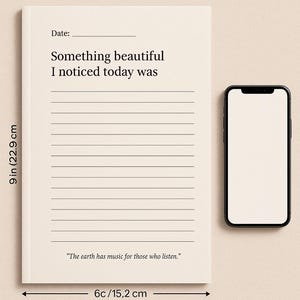 May include: A cream-colored journal with lined pages, measuring 9 inches (22.9 cm) tall and 6 inches (15.2 cm) wide, next to a smartphone. The journal's cover reads "Something beautiful I noticed today was." A quote at the bottom says, "The earth has music for those who listen."