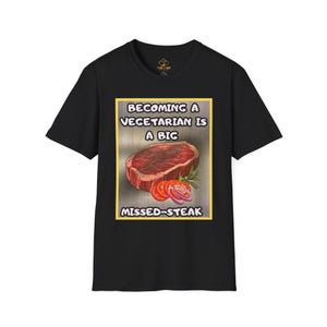 Op de afbeelding: Zwart T-shirt met een afbeelding met de tekst "Becoming a Vegetarian is a Big Missed-Steak". De afbeelding toont een biefstuk, plakjes tomaat en rode uienringen. Het shirt heeft een klassieke ronde hals.