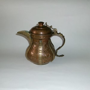 May include: A copper teapot with a brass handle and lid. The teapot is decorated with floral patterns and has a brass band around the middle.
