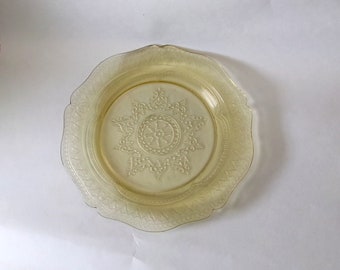May include: A yellow glass plate with a scalloped edge and a raised floral design in the center.