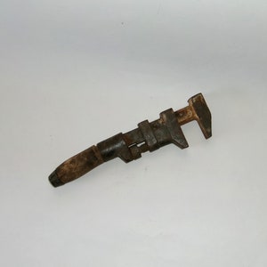 May include: A rusty, old adjustable wrench with a wooden handle. The wrench is made of metal and has a black finish. The handle is made of wood and has a brown finish.
