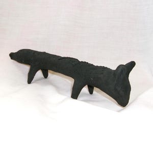 Puede incluir: Escultura negra de un animal con cuatro patas, posiblemente un perro. La obra de arte tiene una superficie rugosa y texturizada y está sobre un fondo blanco. El diseño de la escultura es abstracto y minimalista.