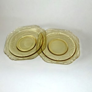 May include: Two yellow glass saucers with a scalloped edge and a delicate floral pattern.