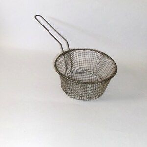 May include: A silver wire mesh frying basket with a long handle. The basket is empty and has a round shape.