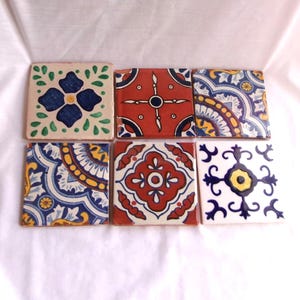 May include: Six square ceramic tiles with colorful, intricate designs. The tiles feature floral and geometric patterns in shades of blue, red, yellow, and white. The tiles are arranged on a white surface.