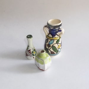 May include: Three small ceramic vases with intricate hand-painted designs. The largest vase is white with blue, green, and yellow floral patterns. The smallest vase is white with green and red floral patterns. The middle vase is green and white with a geometric design.