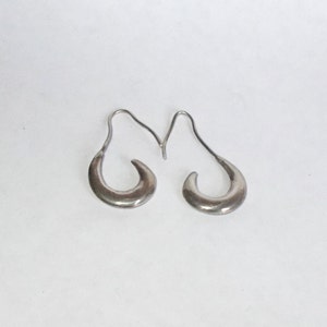 May include: A pair of silver hoop earrings with a curved, crescent moon shape. The earrings are simple and elegant.