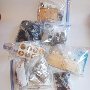 May include: Assortment of buttons in various colors and sizes, packaged in clear plastic bags. Some bags contain buttons with a gold finish, others with a black finish, and others with a mix of colors. The buttons are arranged in a variety of patterns and designs.
