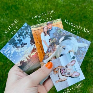May include: A hand holds a collection of square and rectangular photos, labeled "XL FLATIE" (4" x 3"), "Large FLATIE" (3.5" x 2.5"), "Medium FLATIE" (3" x 3"), and "Small FLATIE" (2.5" x 2.5"). The photos feature images of a couple, a dog, and a landscape.