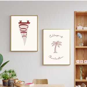 May include: Two framed art prints with gold frames hang on a white wall. One features the text "COFC" in maroon on a pennant shape. The other displays a palm tree illustration and the words "College of Charleston" in maroon.