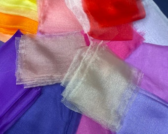 May include: A collection of colorful sheer fabric squares in various shades of pink, purple, blue, green, yellow, orange, and red. The fabric is arranged in a semi-circle pattern, with the lighter colors at the top and the darker colors at the bottom.