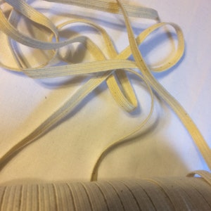 May include: A close-up of a spool of natural cotton elastic cord. The cord is beige and has a slightly textured surface.